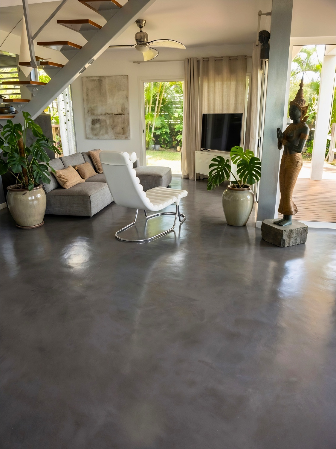 Séjour de villa tropicale au sol en béton minéral gris poli, ouvert sur un jardin de palmiers
